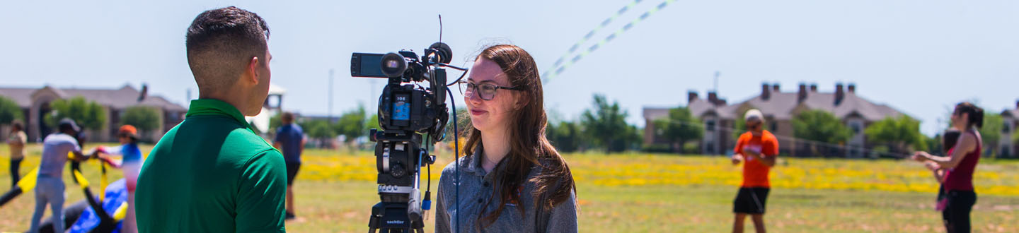 Student interviewing another student on camera on campus at an event