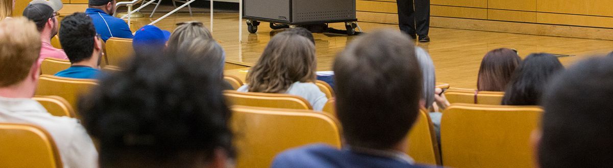 estudiantes sentados en el auditorio escuchando al profesor