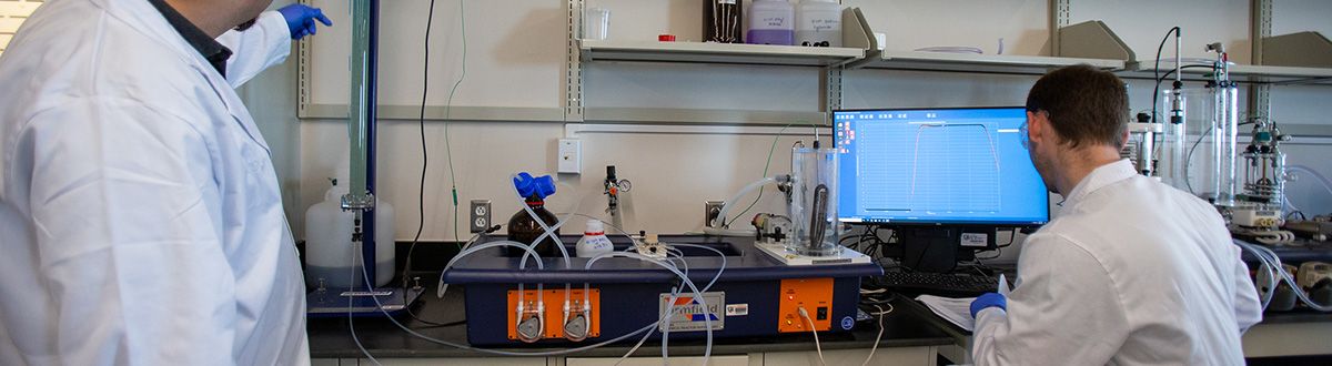 Two male chemical engineers working with machine in chemical engineering laboratory