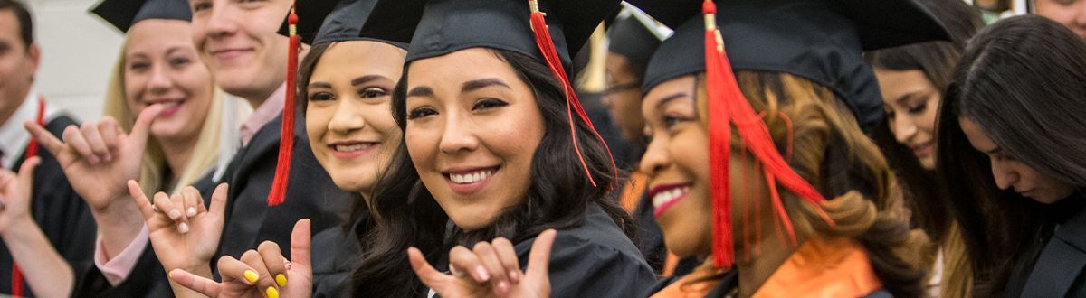 Graduates at graduation smiling and doing the falcons up hand sign