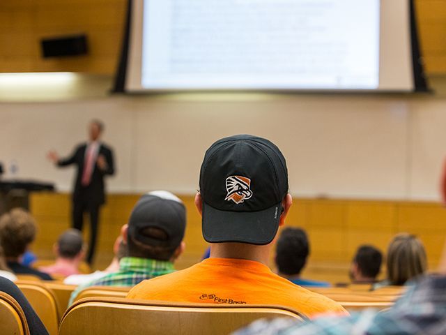students sitting in a lecture, one with UTPB hat on as focus