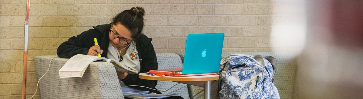 Student studying in the lobby with her books and laptop in a single chair.