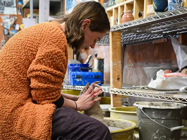 A student throwing and shaping clay into a vase on the pottery wheel.