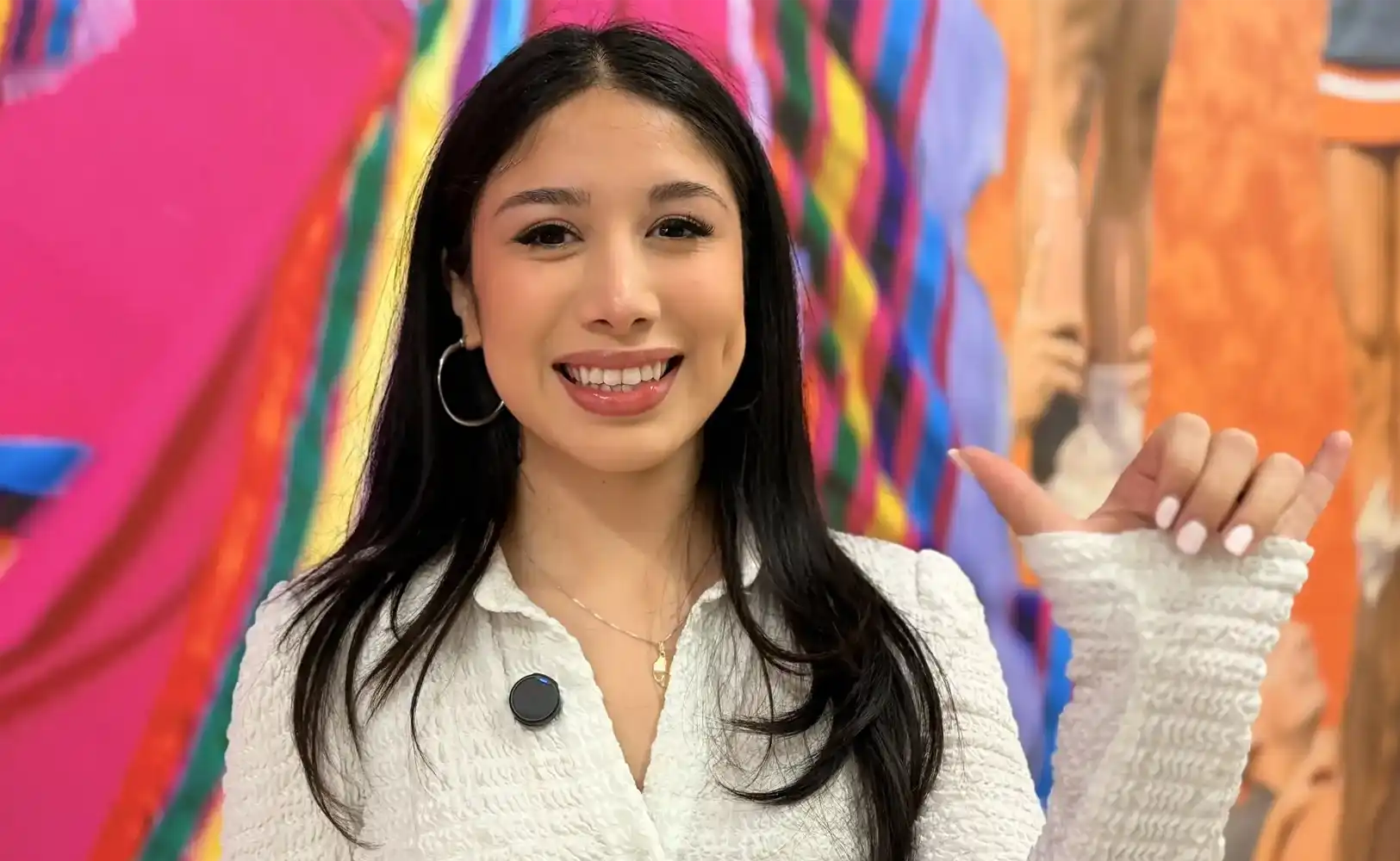 Nathaly Gonzales holding her Falcons Up hand sign by a mural on campus. 