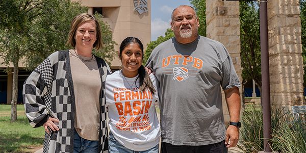 UTPB student, mom, and dad with their arms around each other on campus.
