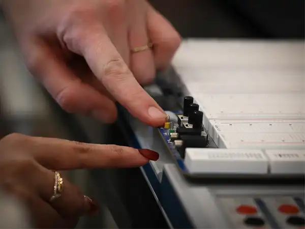Two hands pointing at a bread board, a tool often used by electrical engineering students in labs to test circuits.