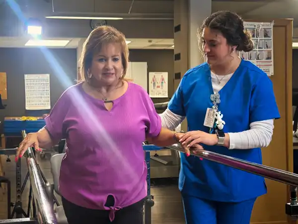 A physical therapist assisting a patient walking with support bars.