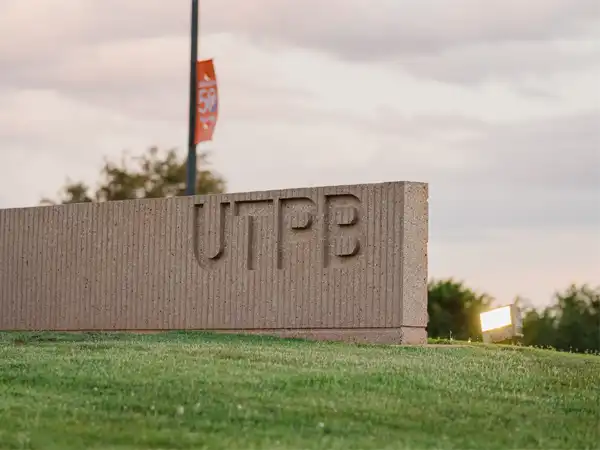 A photo of a sunrise on the UTPB campus with an entrance maker of stone with the letters UTPB engraved into the stone.
