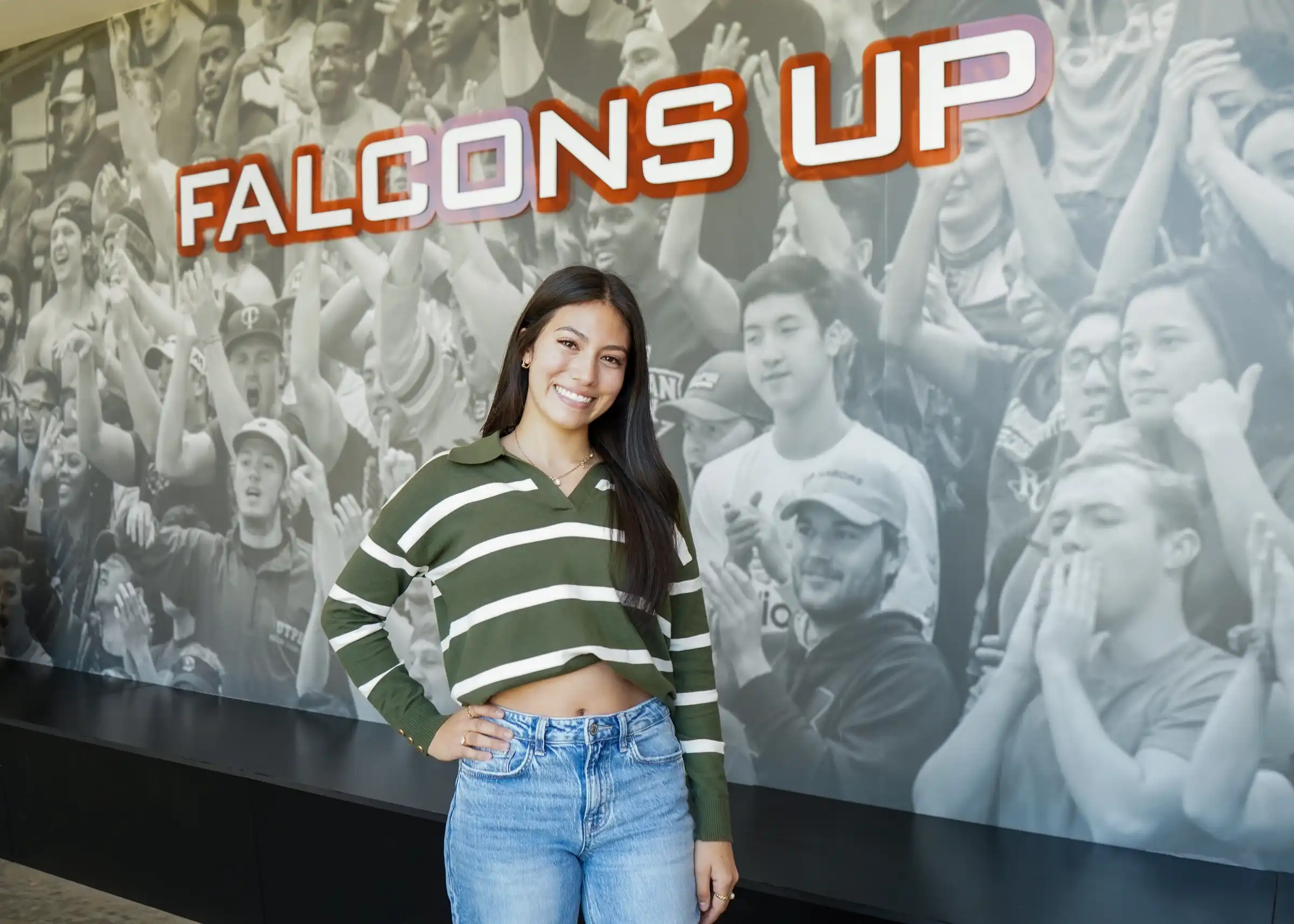Lindsey Ruiz standing with a Falcons Up sign on campus. 