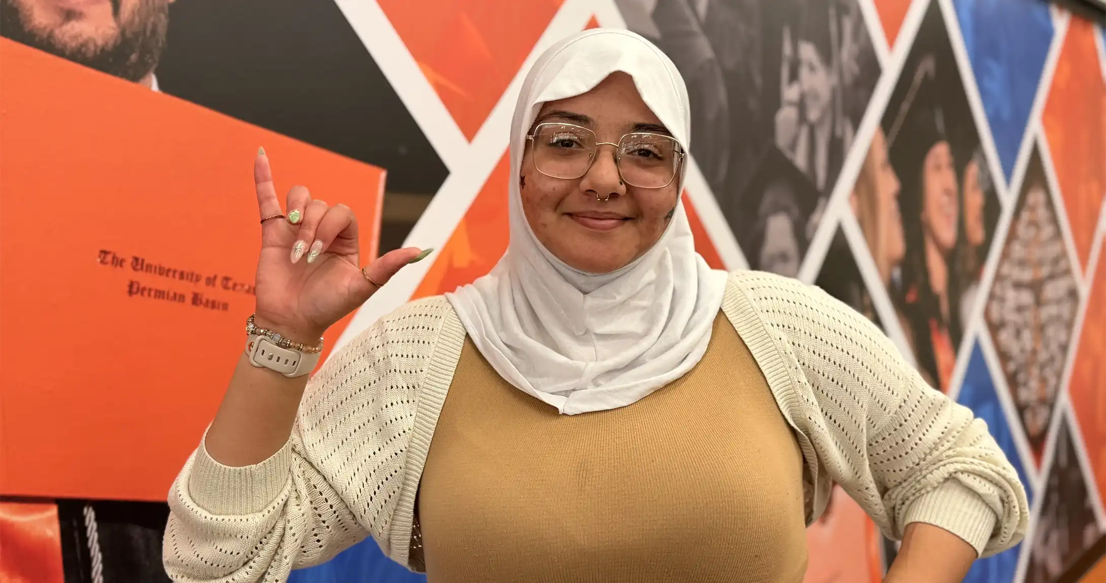 Areej Khodair holding the "Falcons Up" hand sign in front of a mural on campus.
