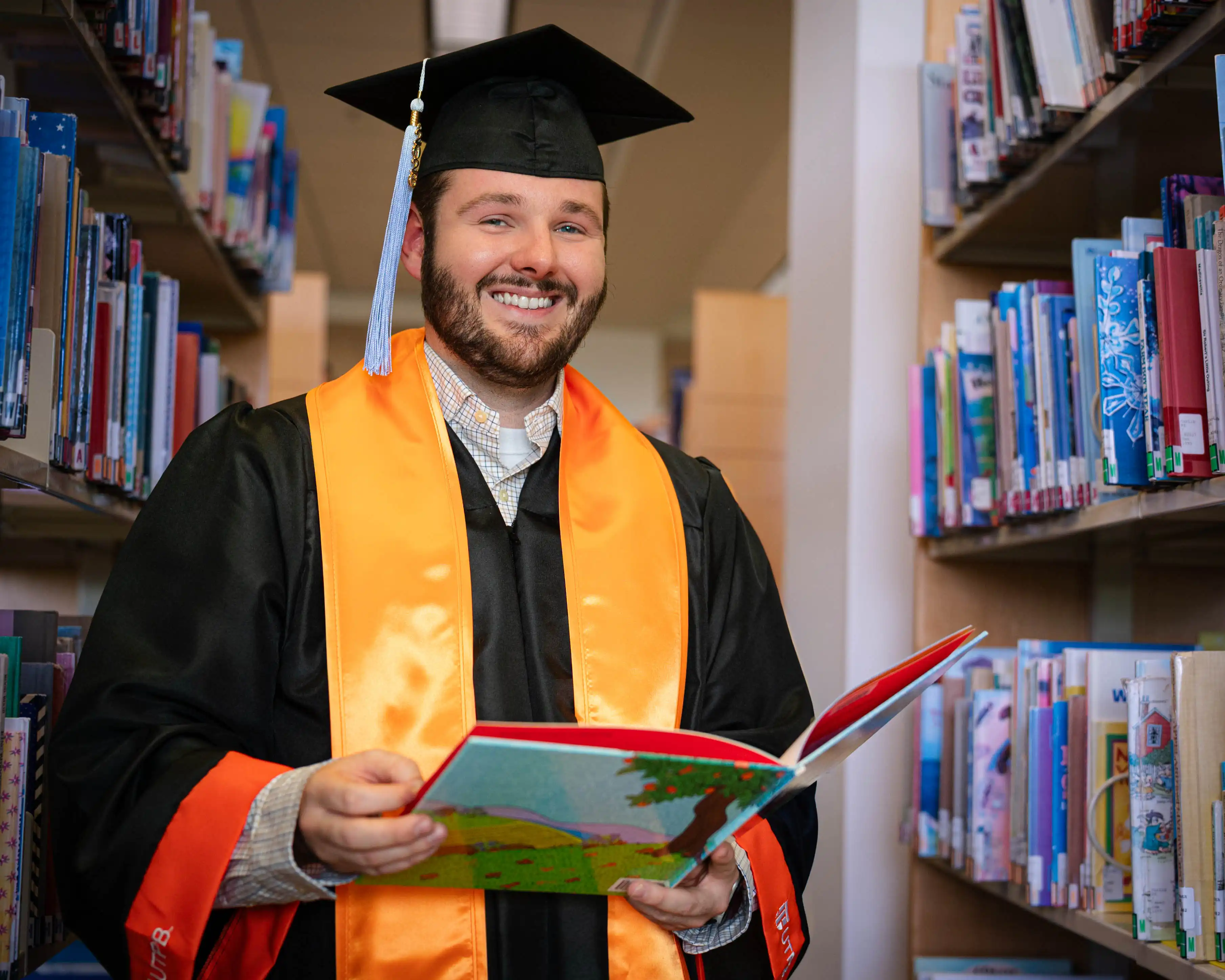 Brandon Rolston holding a children's book in the UTPB library. 