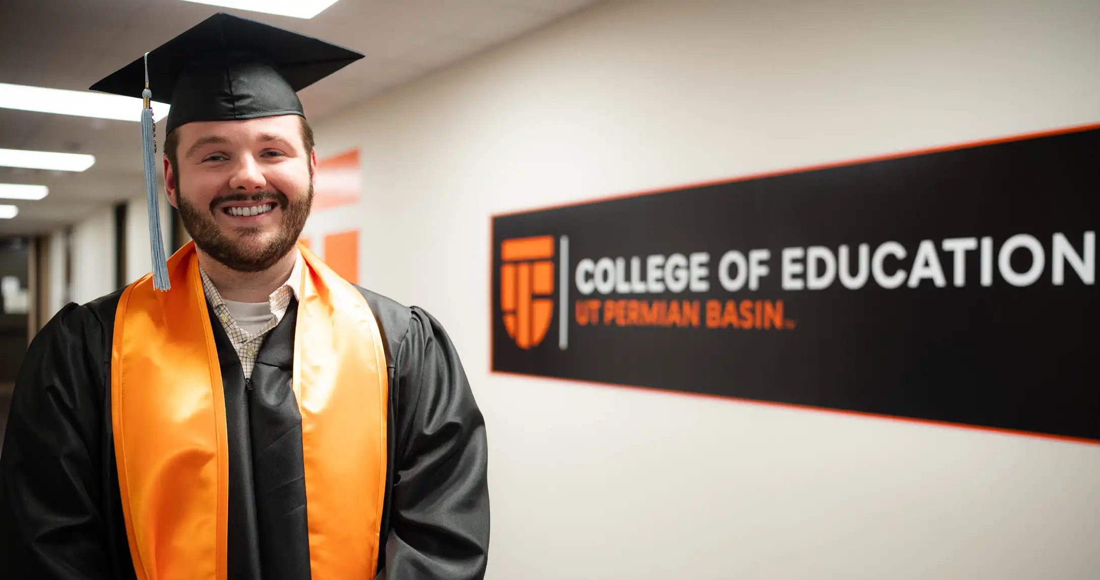 UTPB graduate Brandon Rolston standing in front of a College of Education sign on UTPB's campus. 