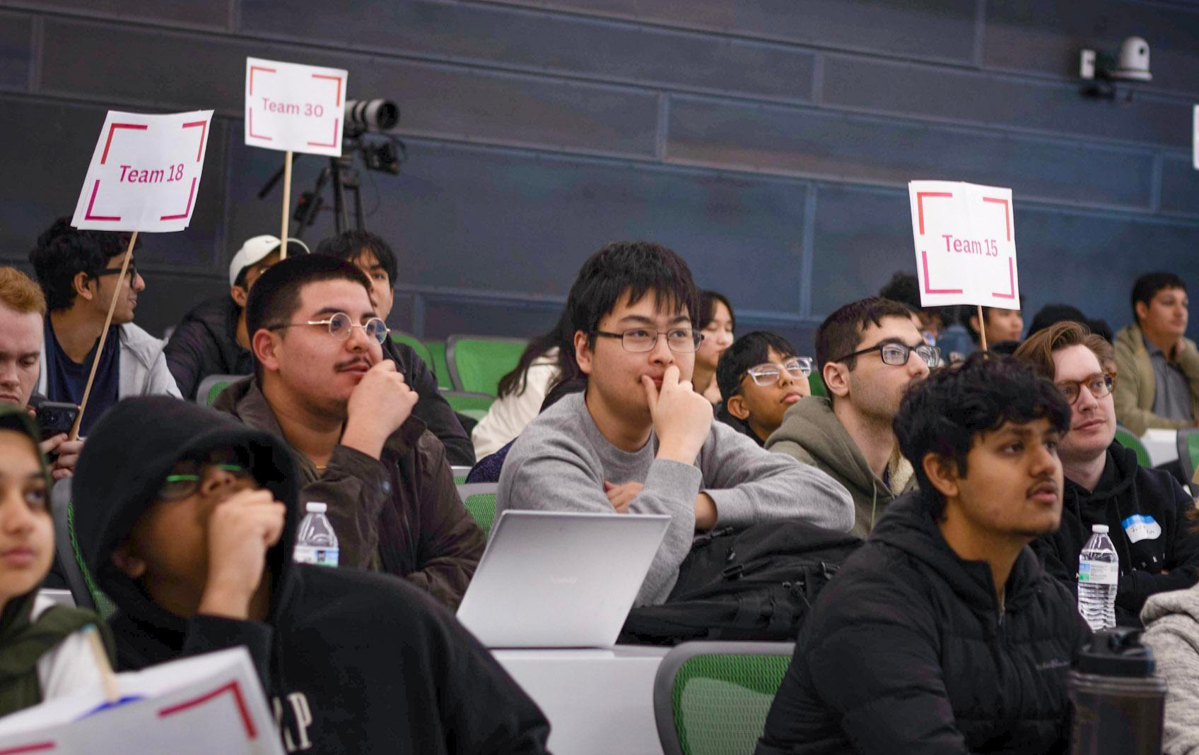 Four computer science students from UTPB sitting in a lecture hall at the Axxess Hackathon among other competitors. 