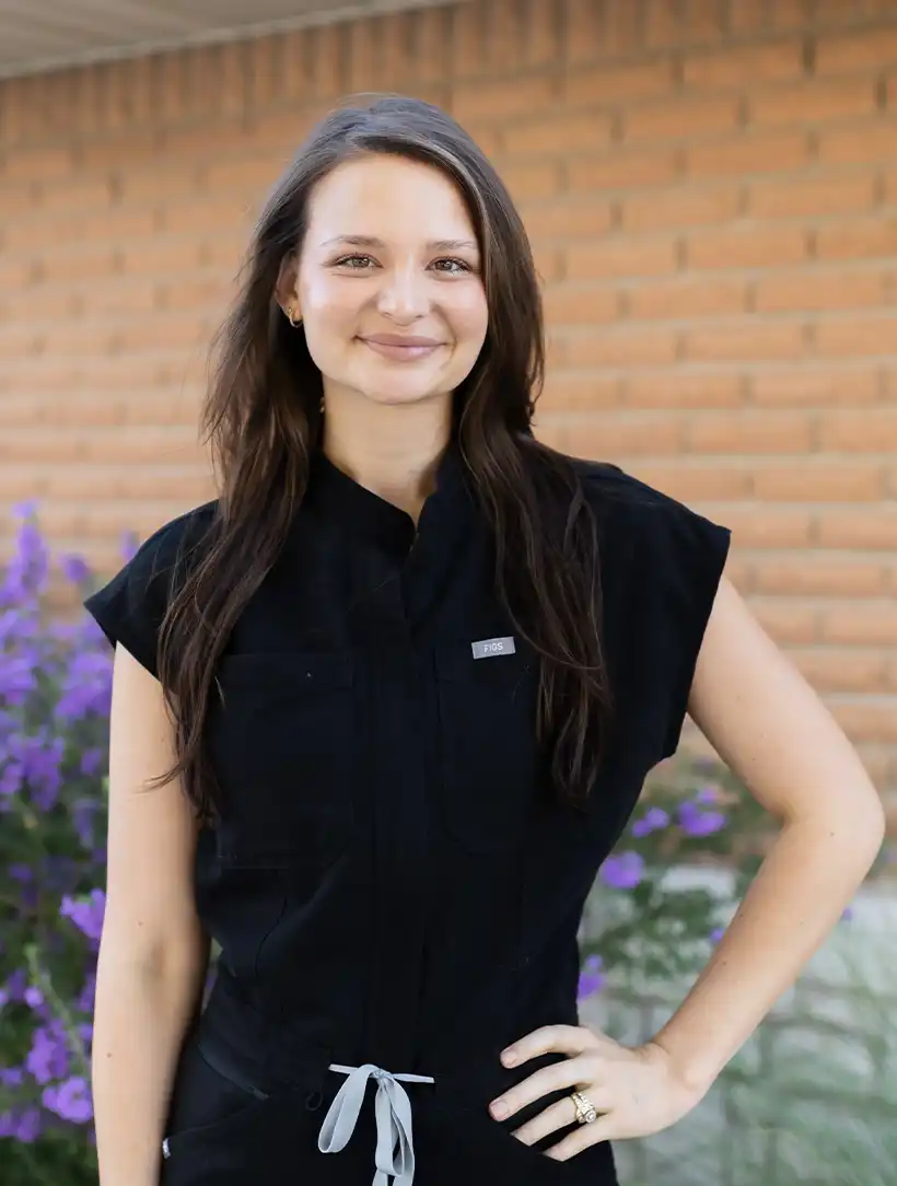 Heather smiling outdoors in black medical scrubs.