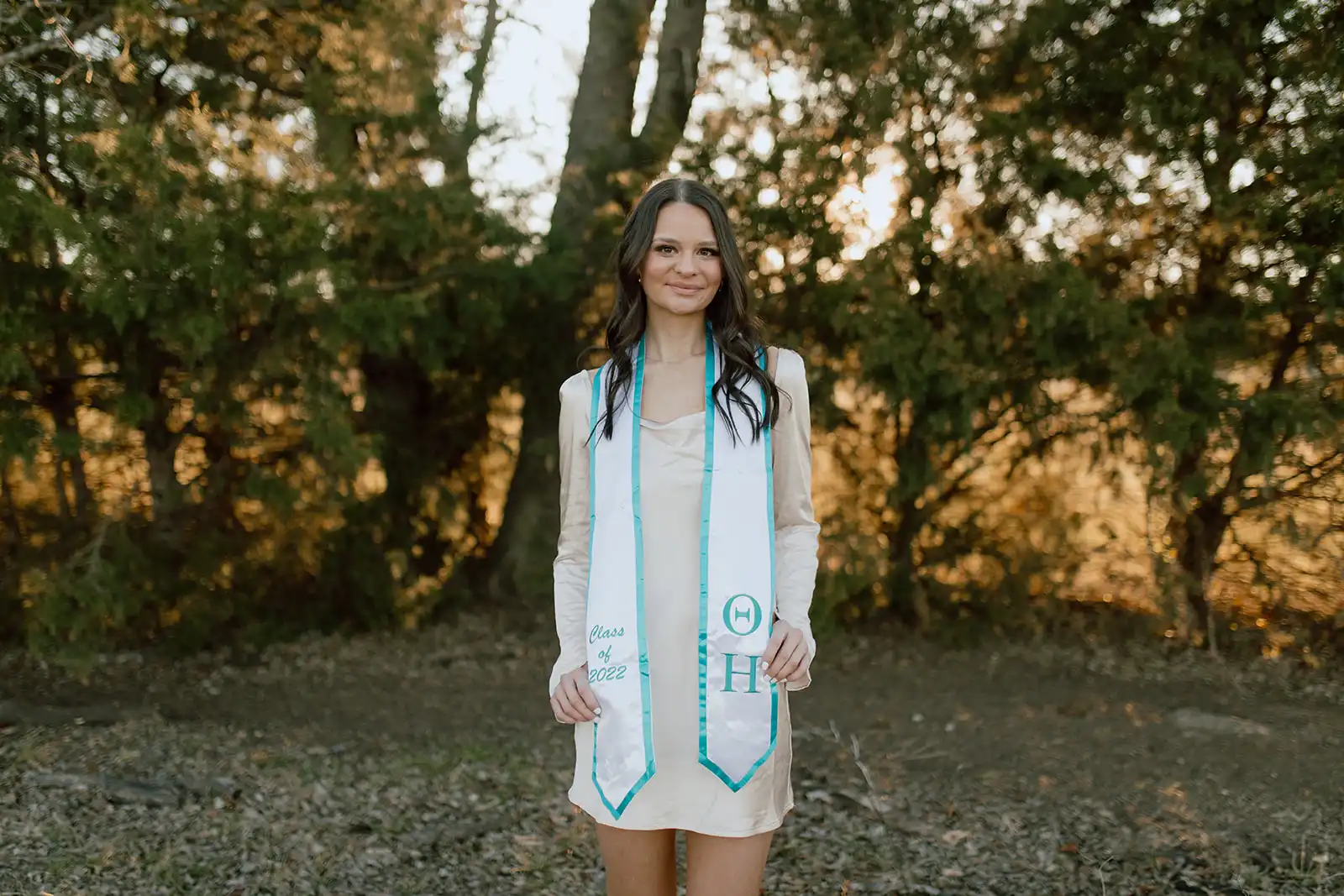 Heather in front of some trees outside, with her sorority's graduation stole. 
