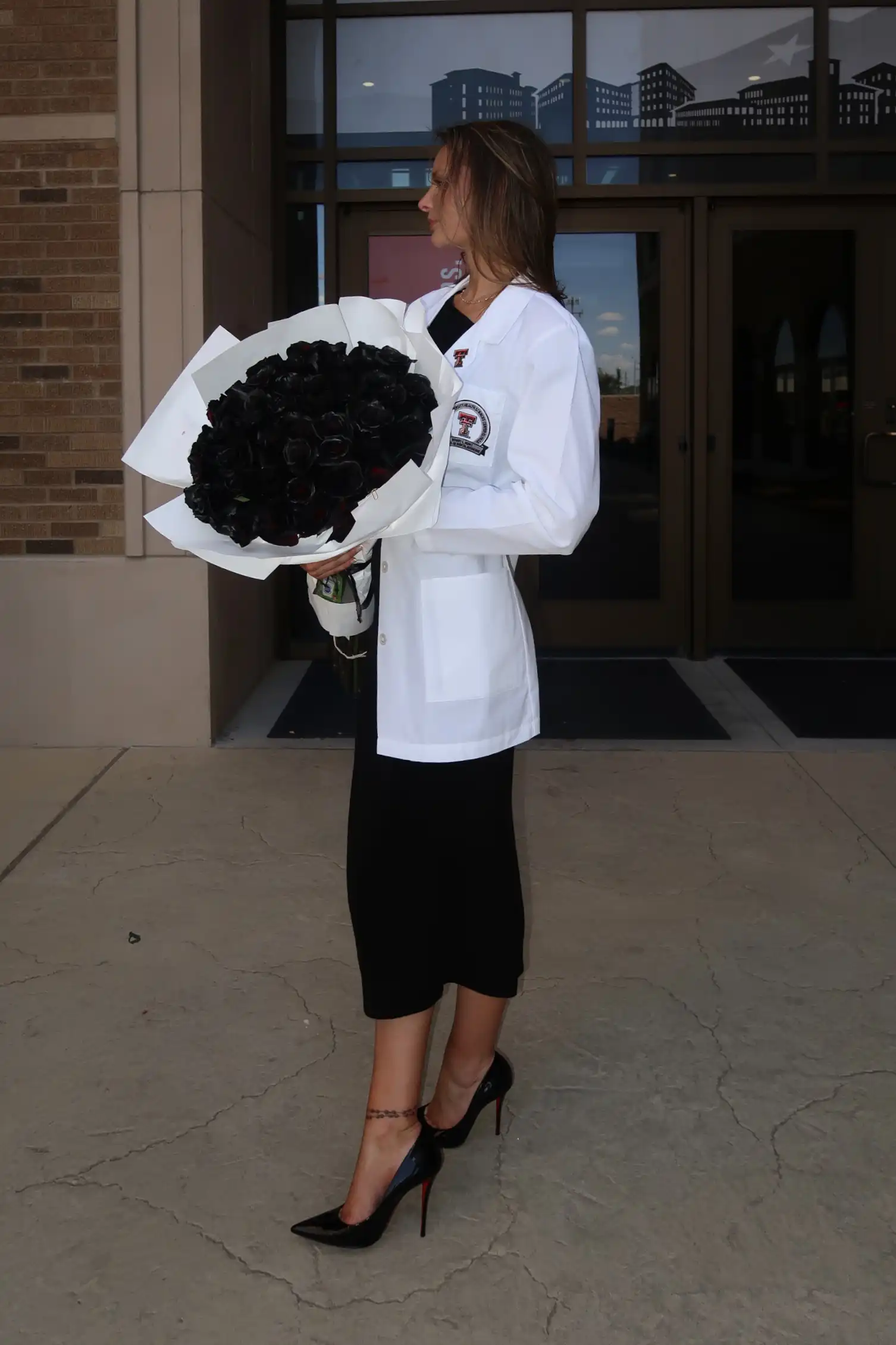 Heather wearing a white coat and holding a bouquet of black roses.ental white coat ceremony. 