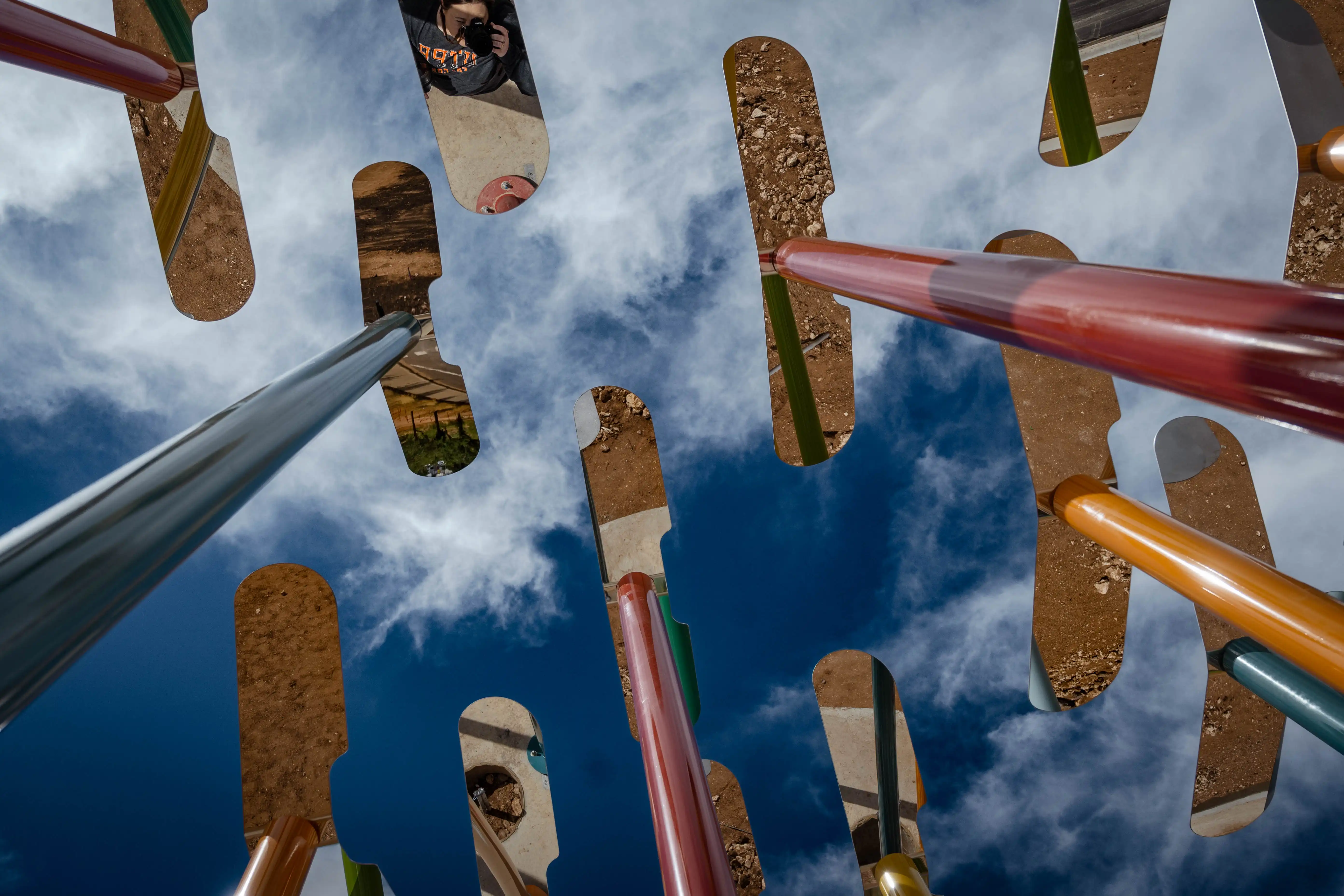 A variety of colorful metal poles, with mirrored metal birds atop them from the view of standing right below them