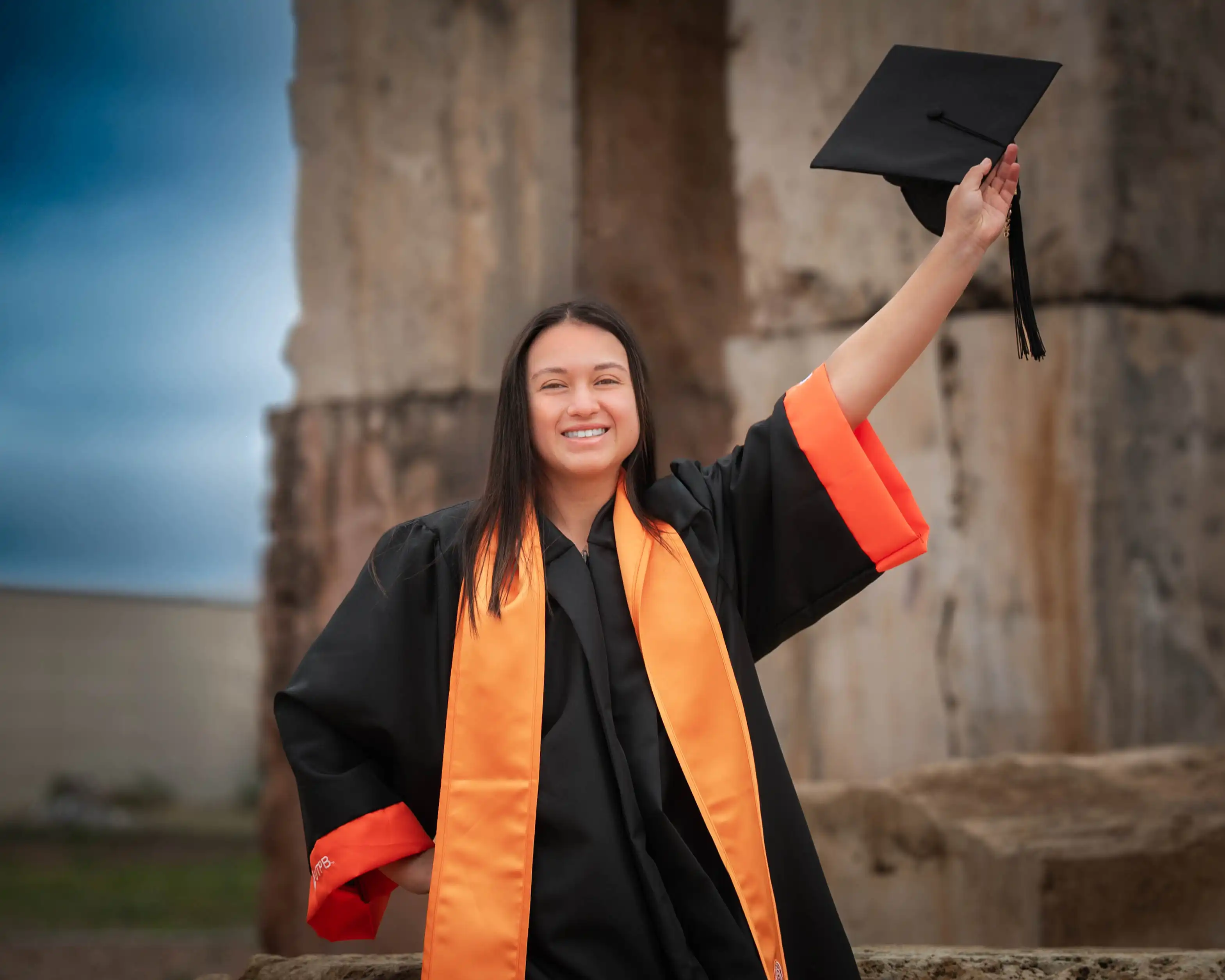 Maria Tarrago in her graduation regalia holding her cap in air. 