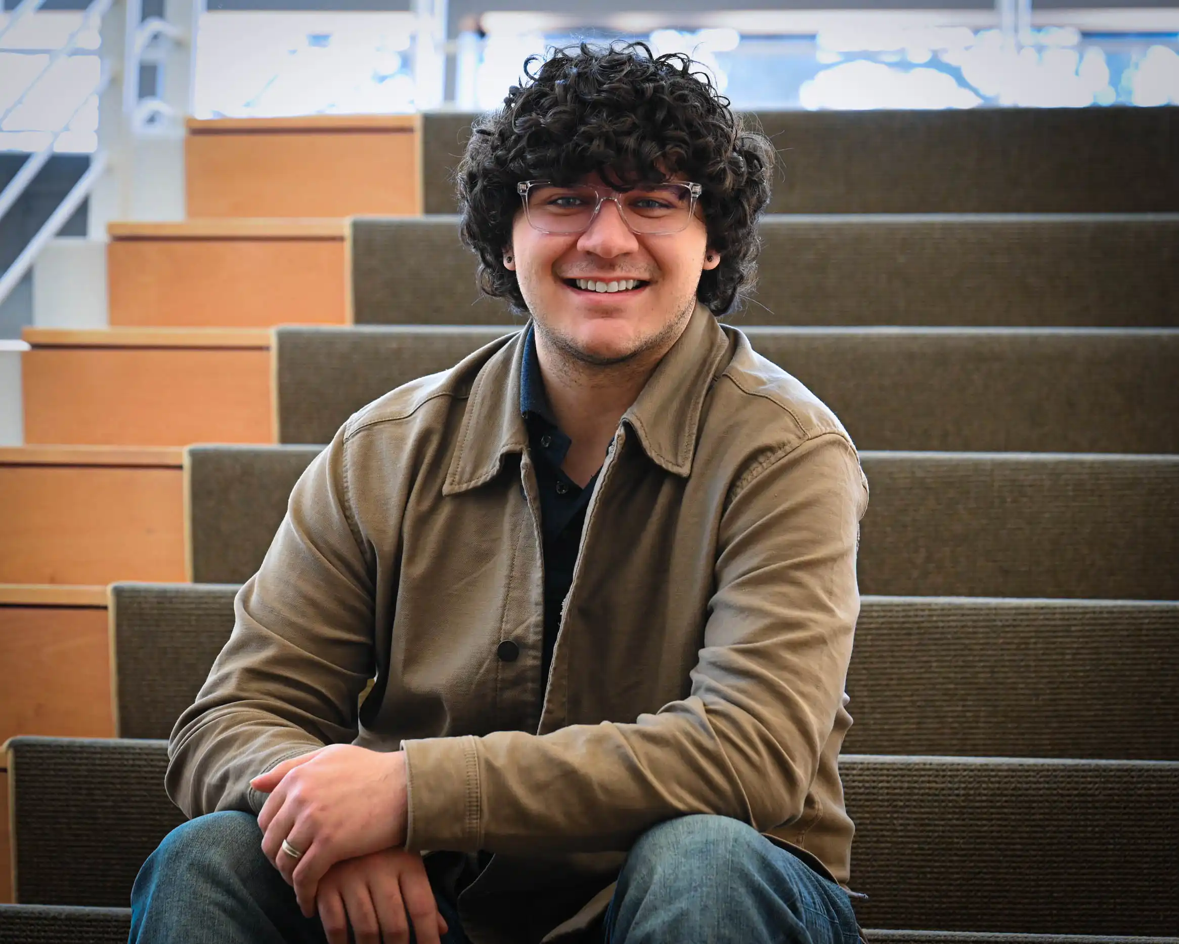 UTPB grad Phillip Driscoll sitting on stairs in the on-campus library. 