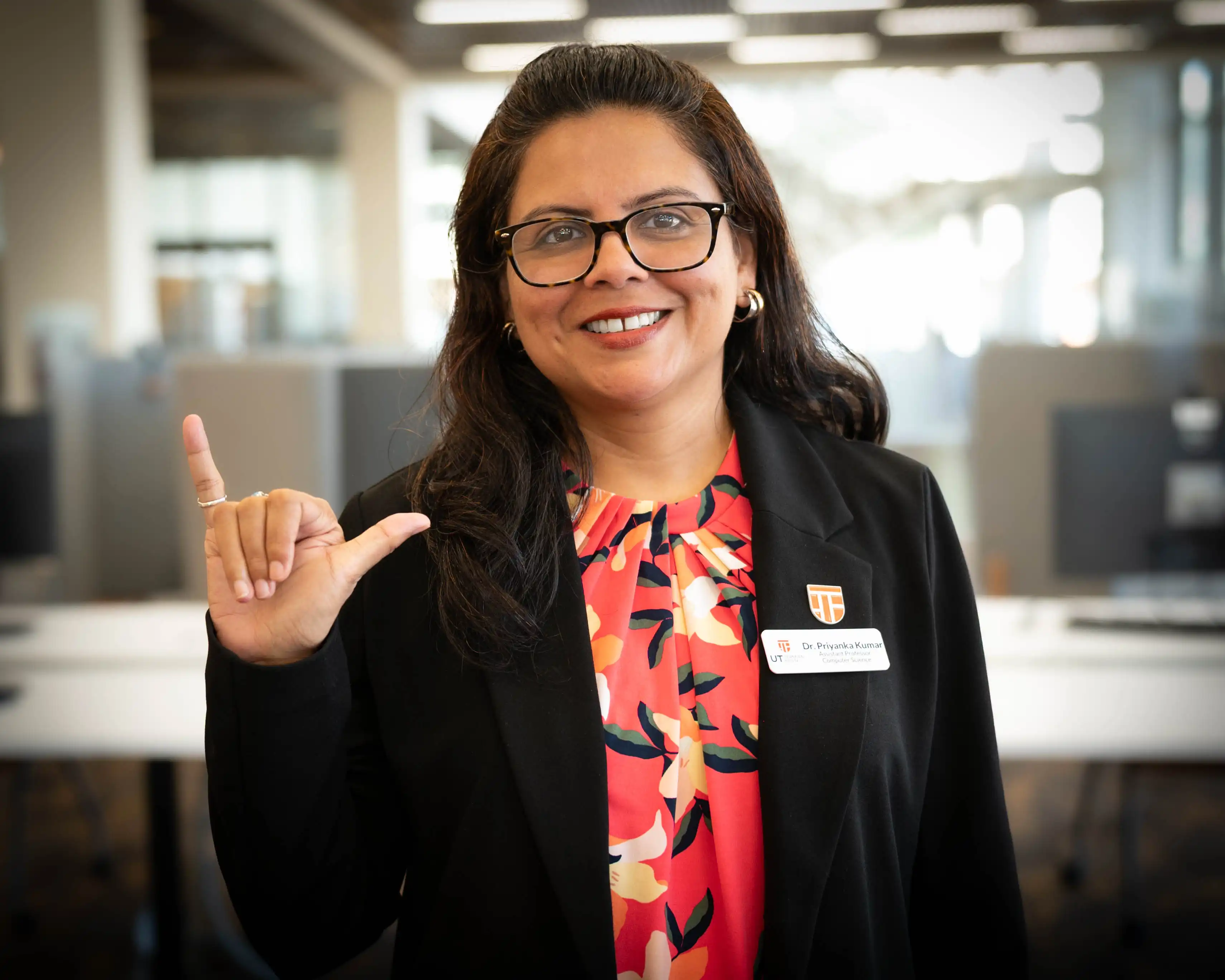 UTPB professor Dr. Priyanka Kumar holding Falcons Up hand sign in the UTPB library. 