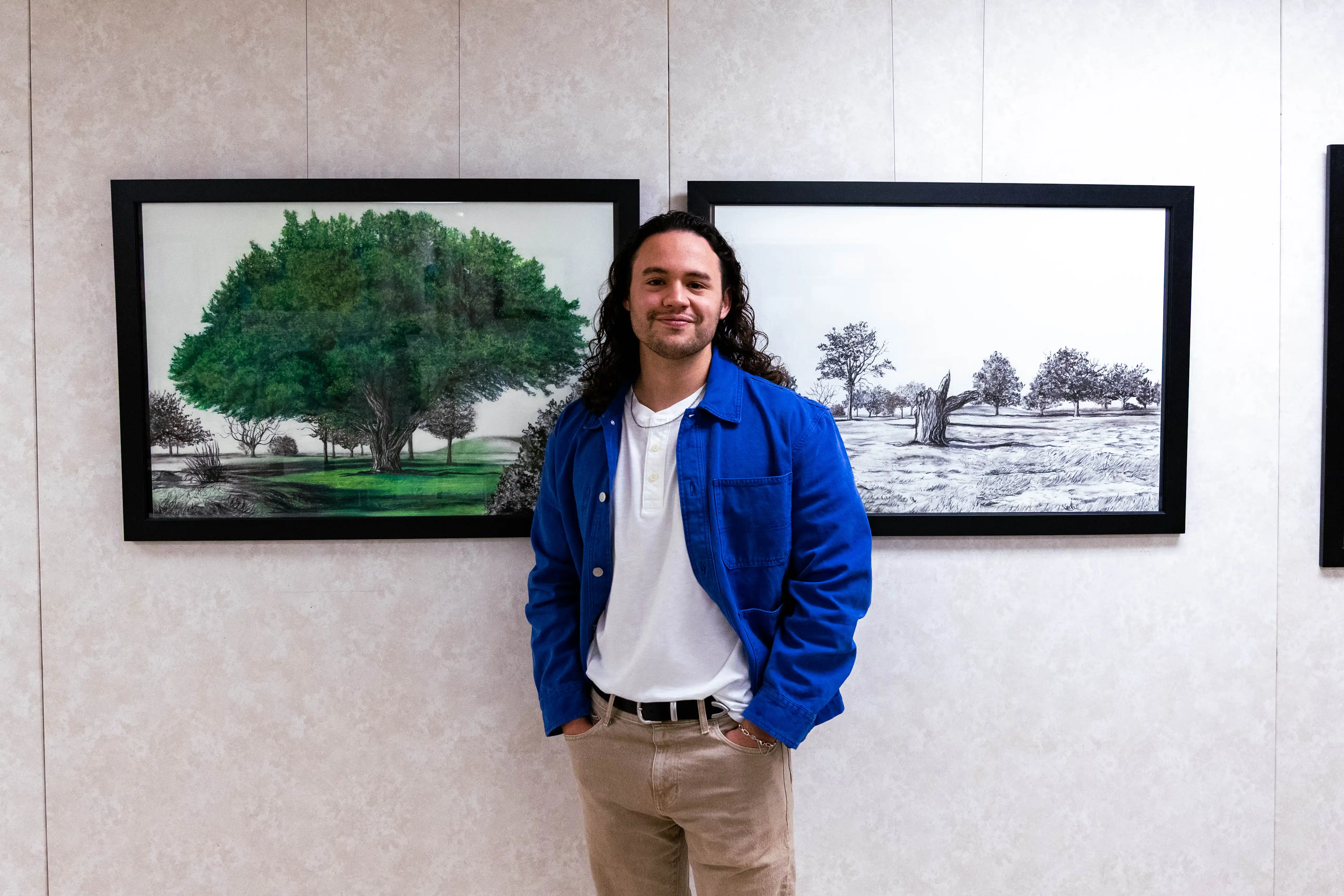 Artists Talon Cress standing in front of his landscape of a tree, before and after it was cut down. The piece was created with charcoal, made from the twigs and bark of the tree.