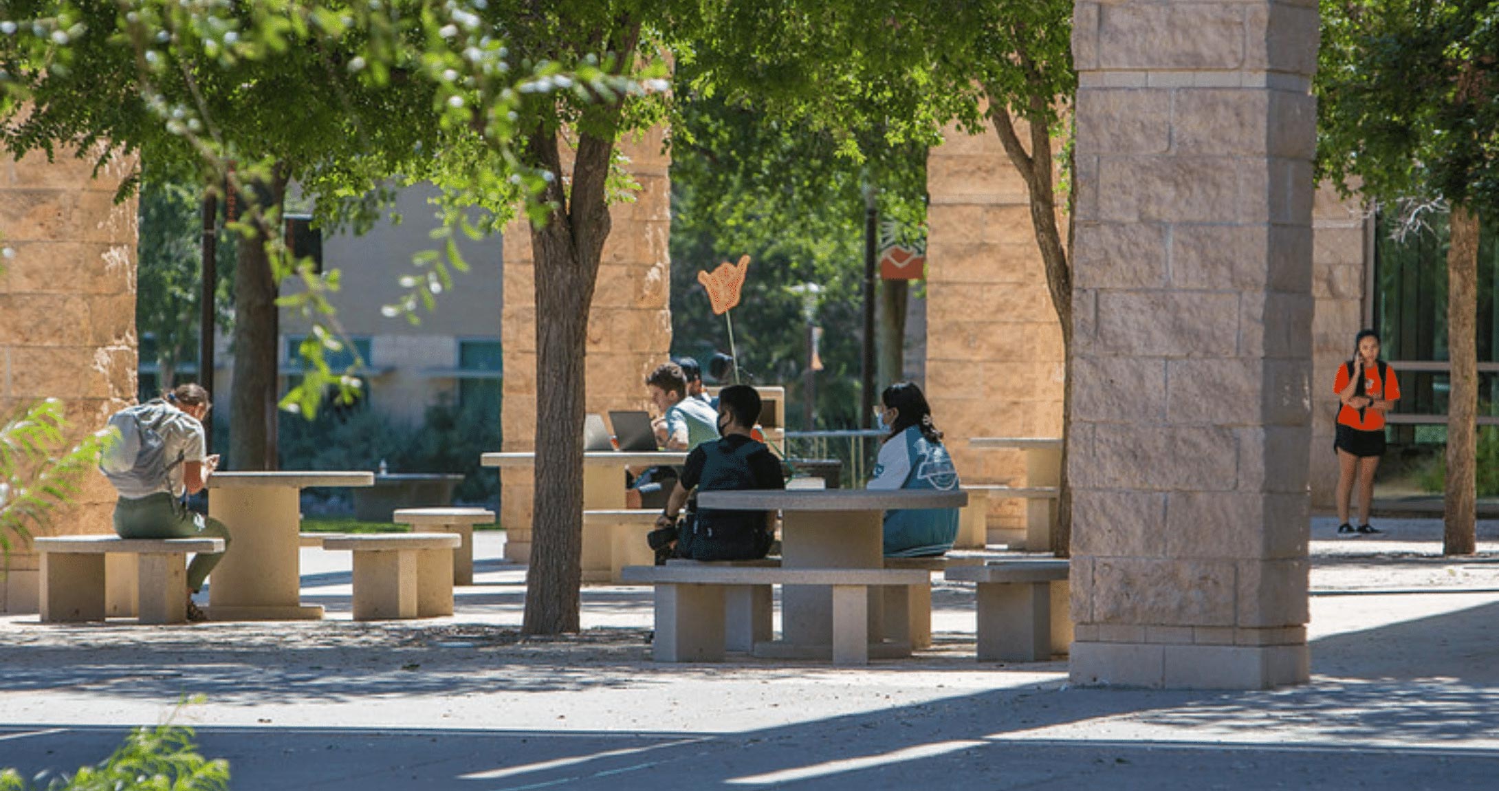 Estudiantes sentados en mesas de picnic al aire libre en el campus