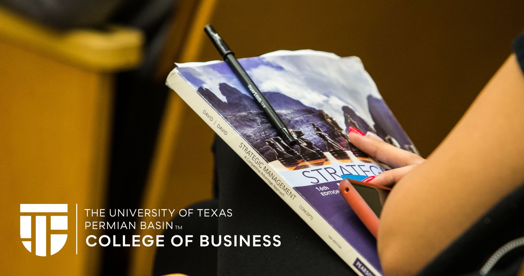 business textbook held by female student in an auditorium seat