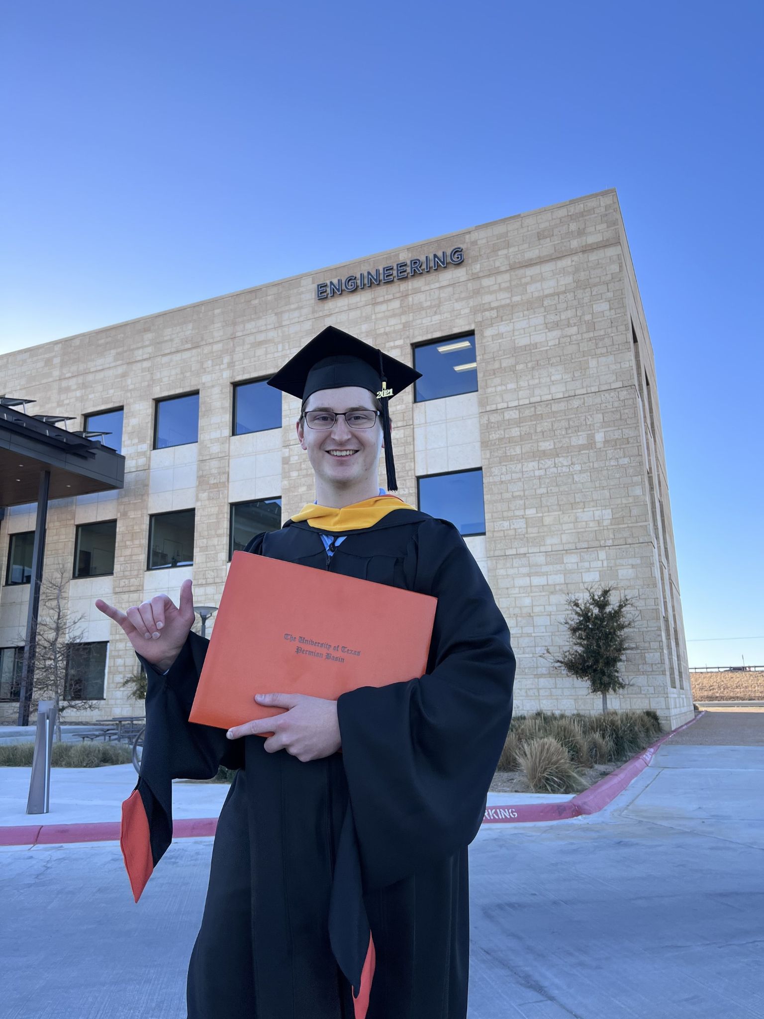 Nolan Hines in front of Engineering Building with diploma, cap and gown