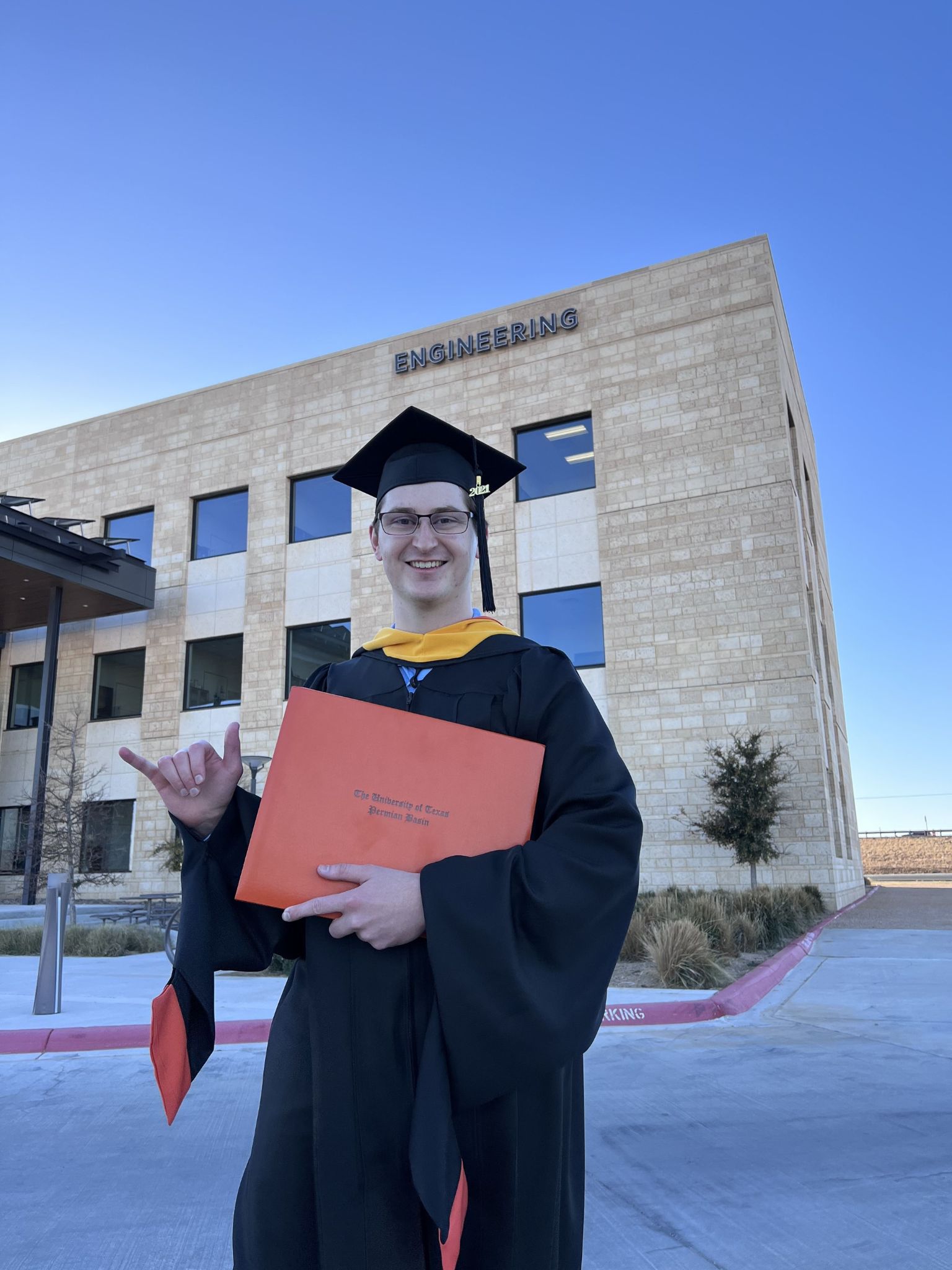 Nolan Hines frente al edificio de ingeniería con diploma, toga y birrete