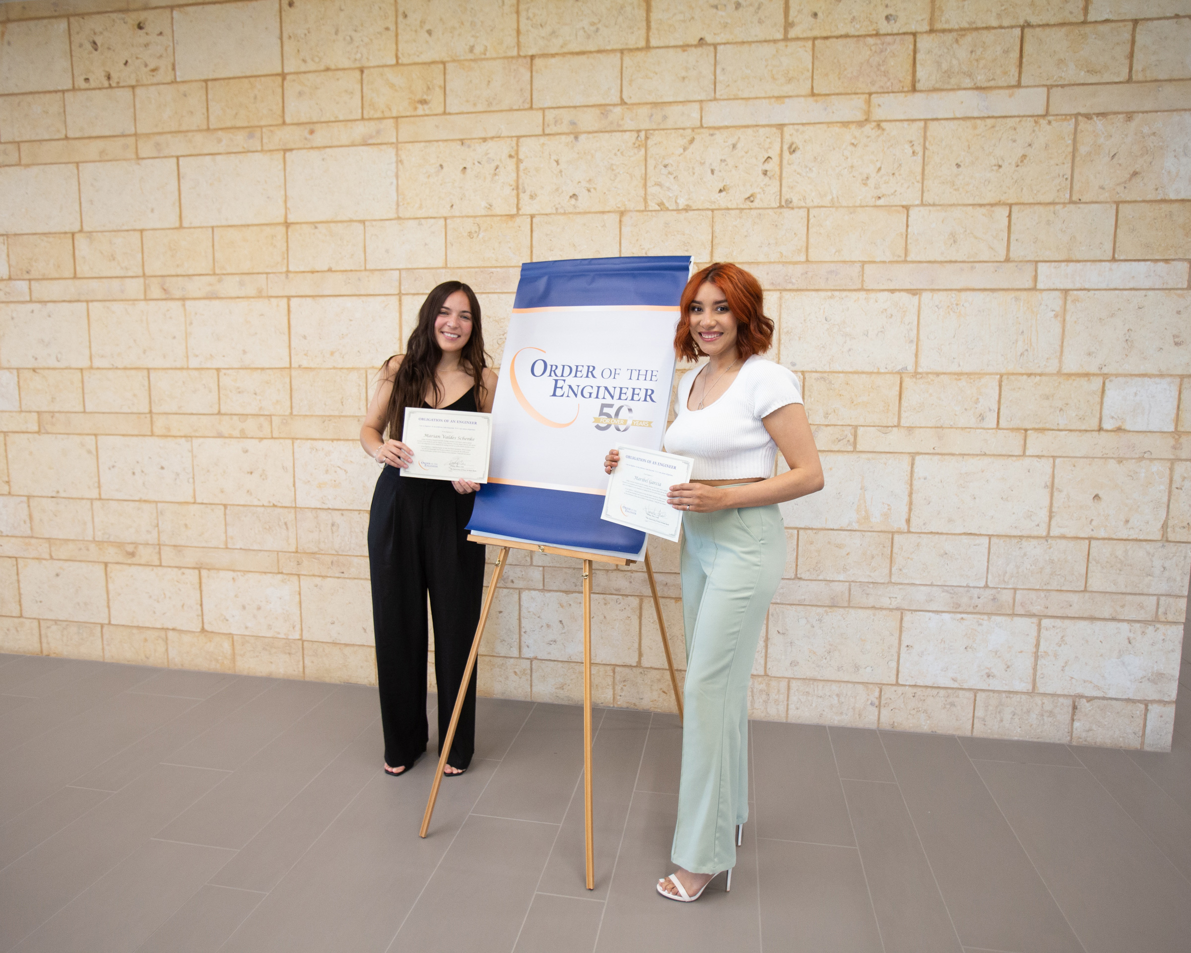 Dos estudiantes de ingeniería posando con certificados de la Orden del Ingeniero