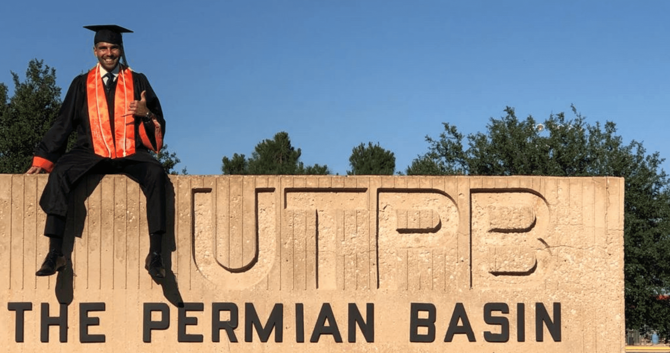 Graduate sitting on rock smiling