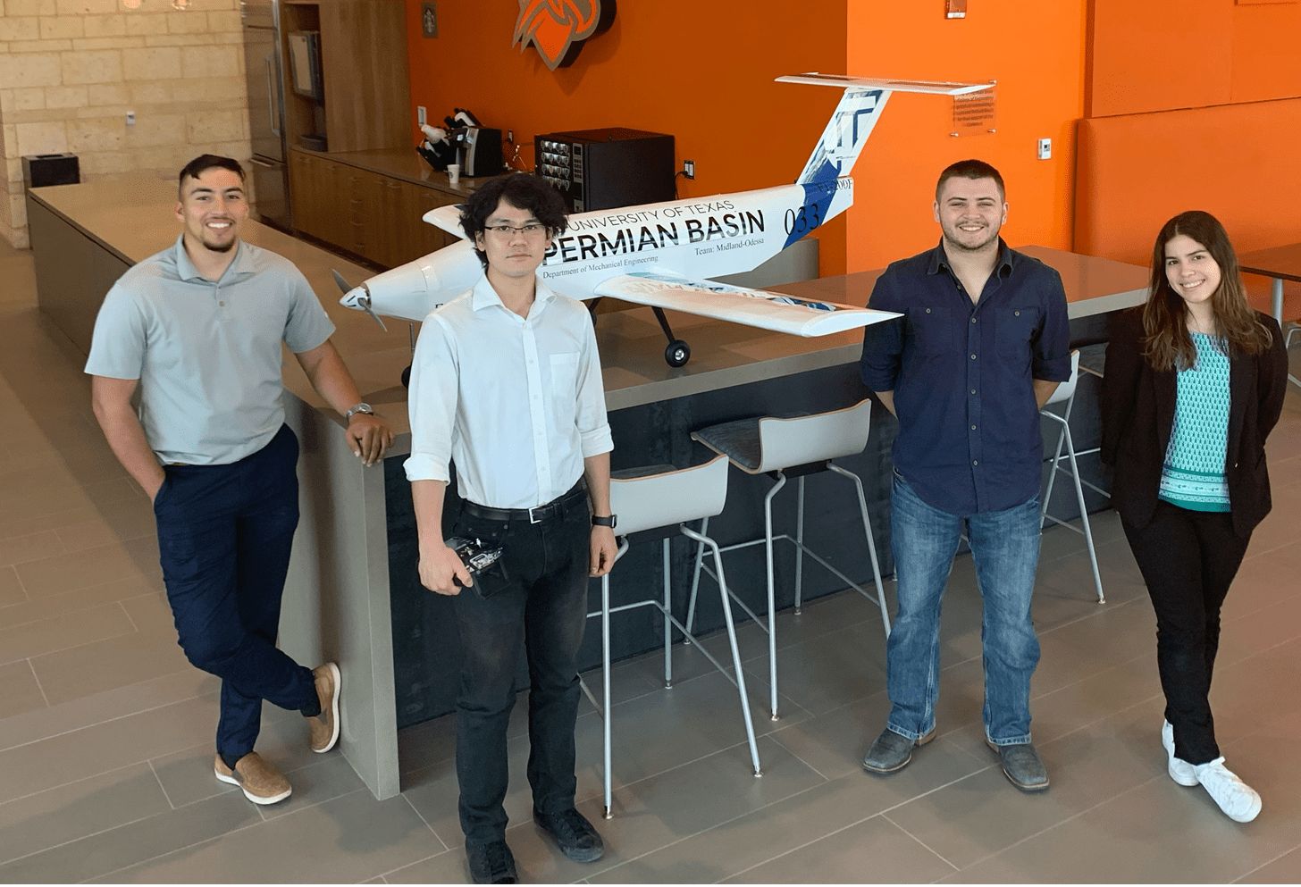 Engineering students posed in engineering building with airplane they designed